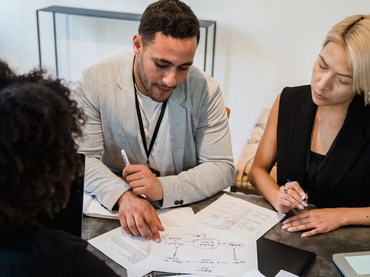Three colleagues at a desk reviewing a printed delivery workflow diagram together